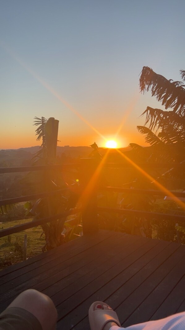 Vista al tramonto da un pontile di legno con ringhiera, palme e una catena montuosa in lontananza.