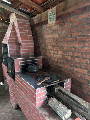 Un'area cucina esterna in mattoni con un camino, una pentola sul fuoco e un cartello appeso al muro.