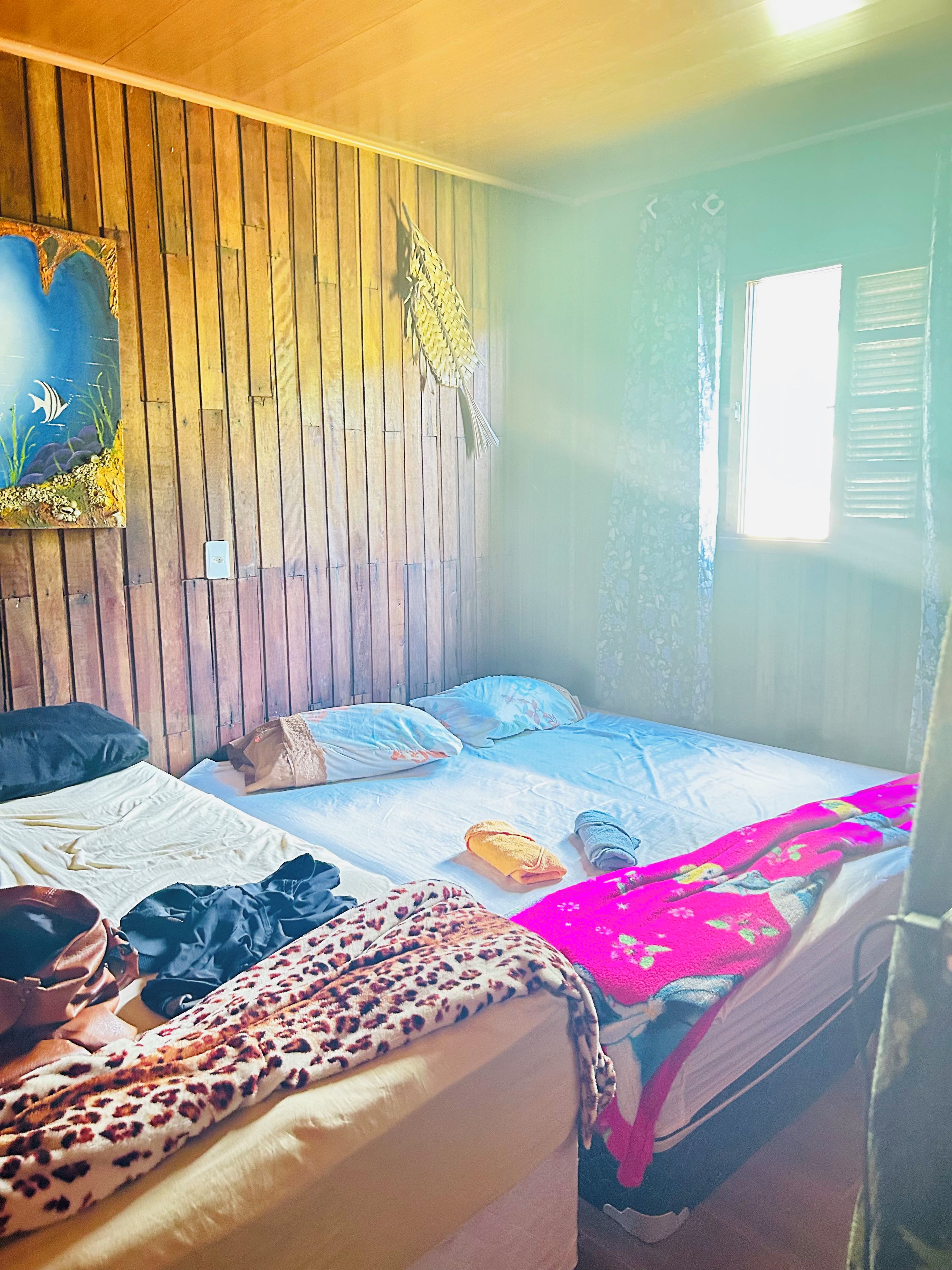 Een kamer met twee bedden, houten wanden, een raam met luiken en een schilderij aan de muur.