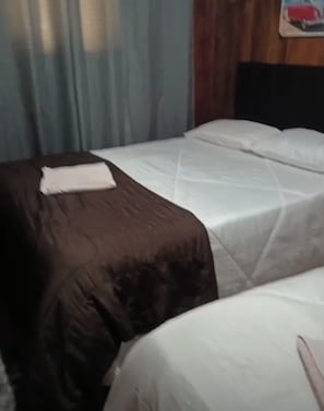 Habitación de hotel con dos camas, una con cubrecolor marrón y la otra con funda blanca.