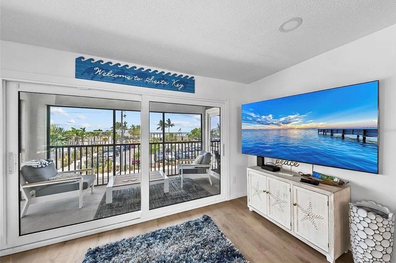 A living room with a large TV, a balcony with a view of the sea, and a welcome sign.