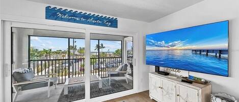 A living room with a large TV, a balcony with a view of the sea, and a welcome sign.