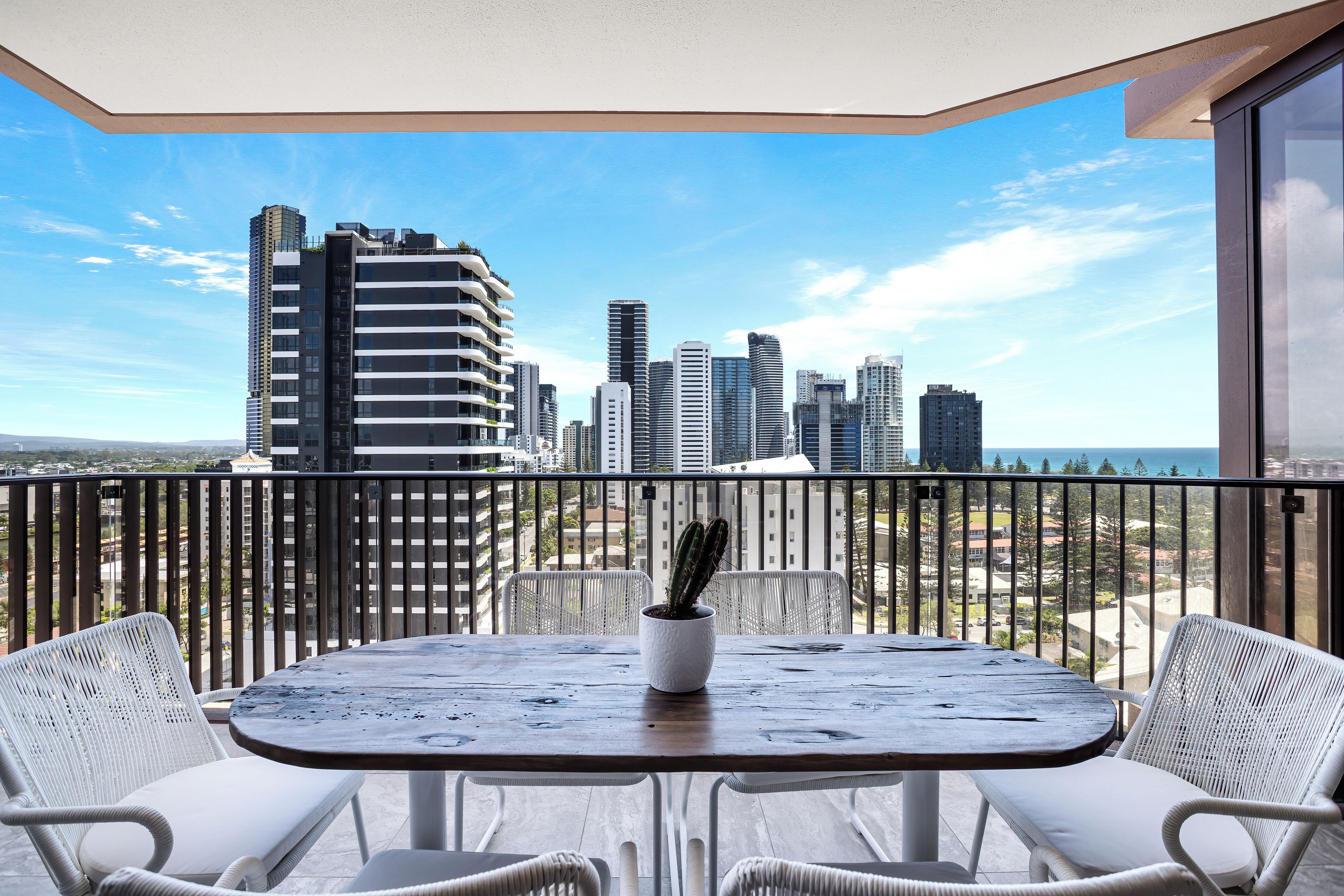 Un balcon donnant sur le panorama urbain, une table avec des chaises et un cactus en pot.