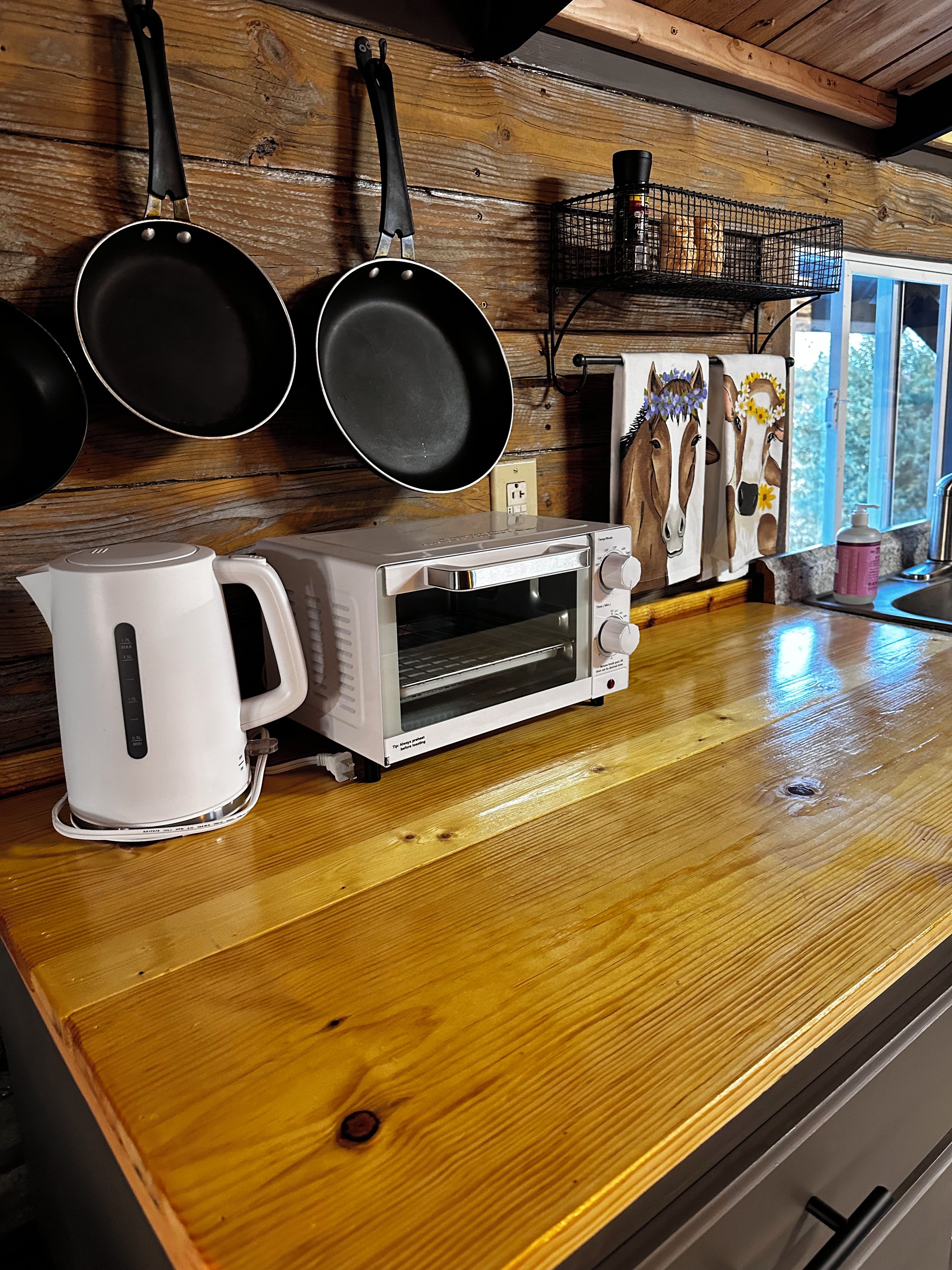 A kitchen with a white toaster oven, a kettle, and hanging pans on the wall.