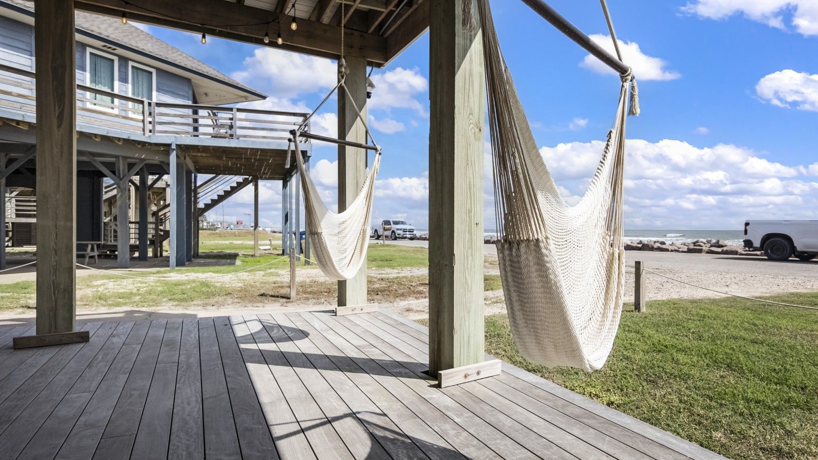A wooden deck with a hammock, a covered area with a railing, and a view of the beach and ocean.