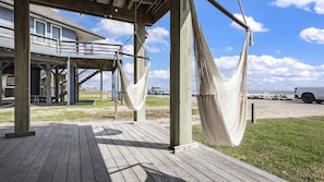 En træterrasse med hængekøje, et overdækket område med gelænder og udsigt til strand og hav.