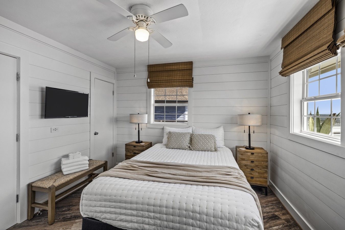 A bedroom with a bed, bedside tables, a television, a ceiling fan, and a window with a view.