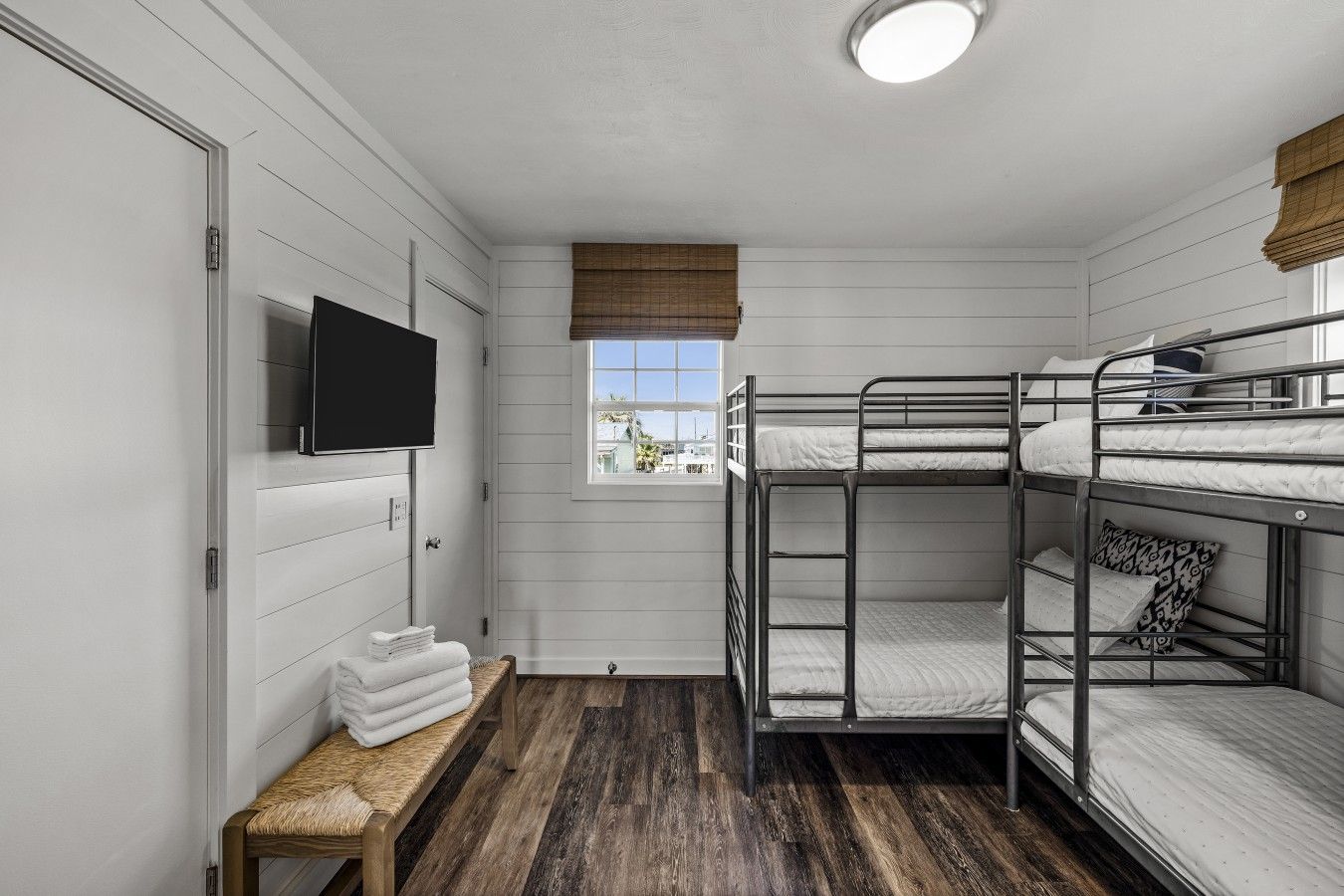 A bunk bed room with a television, a window with a view, and a bench with towels.