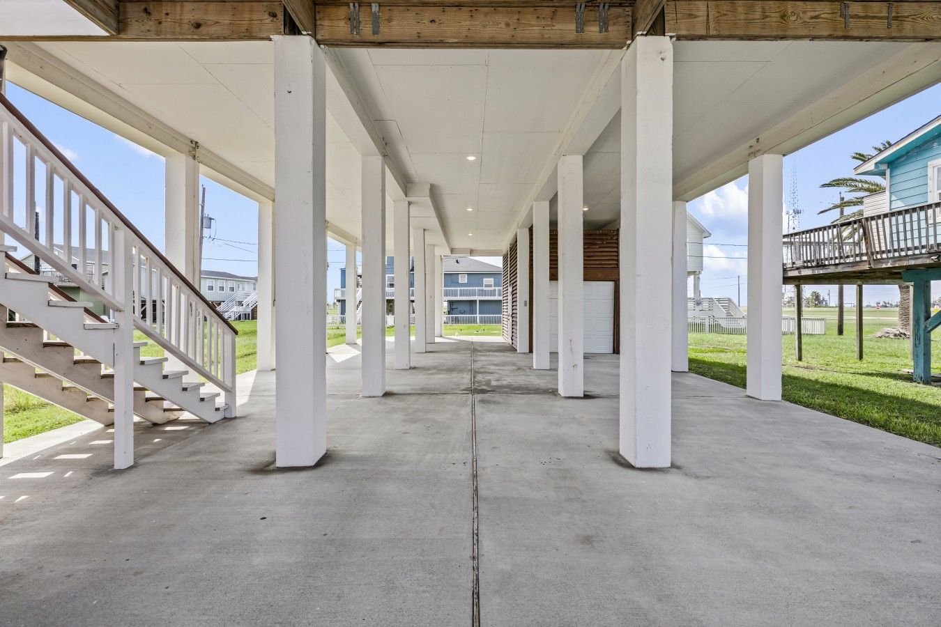 A covered walkway with white pillars, a concrete floor, and a staircase on the left.