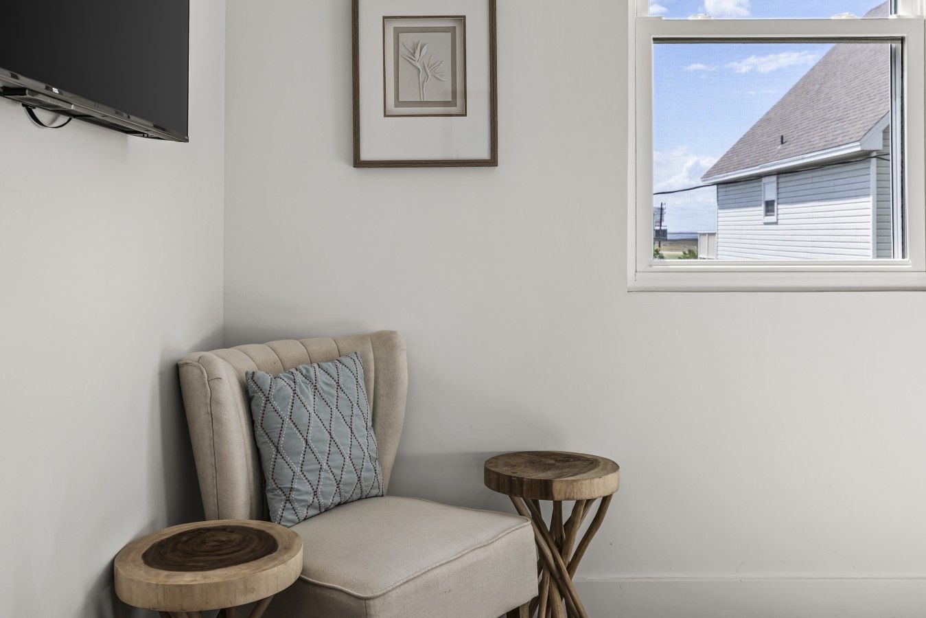 A corner room with a chair, a framed picture, and a window with a view of a house.