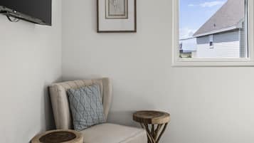 A corner room with a chair, a framed picture, and a window with a view of a house.