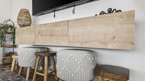 Een moderne woonkamer met een houten tv-meubel, twee grijze gestoffeerde krukken en een geweven mand.