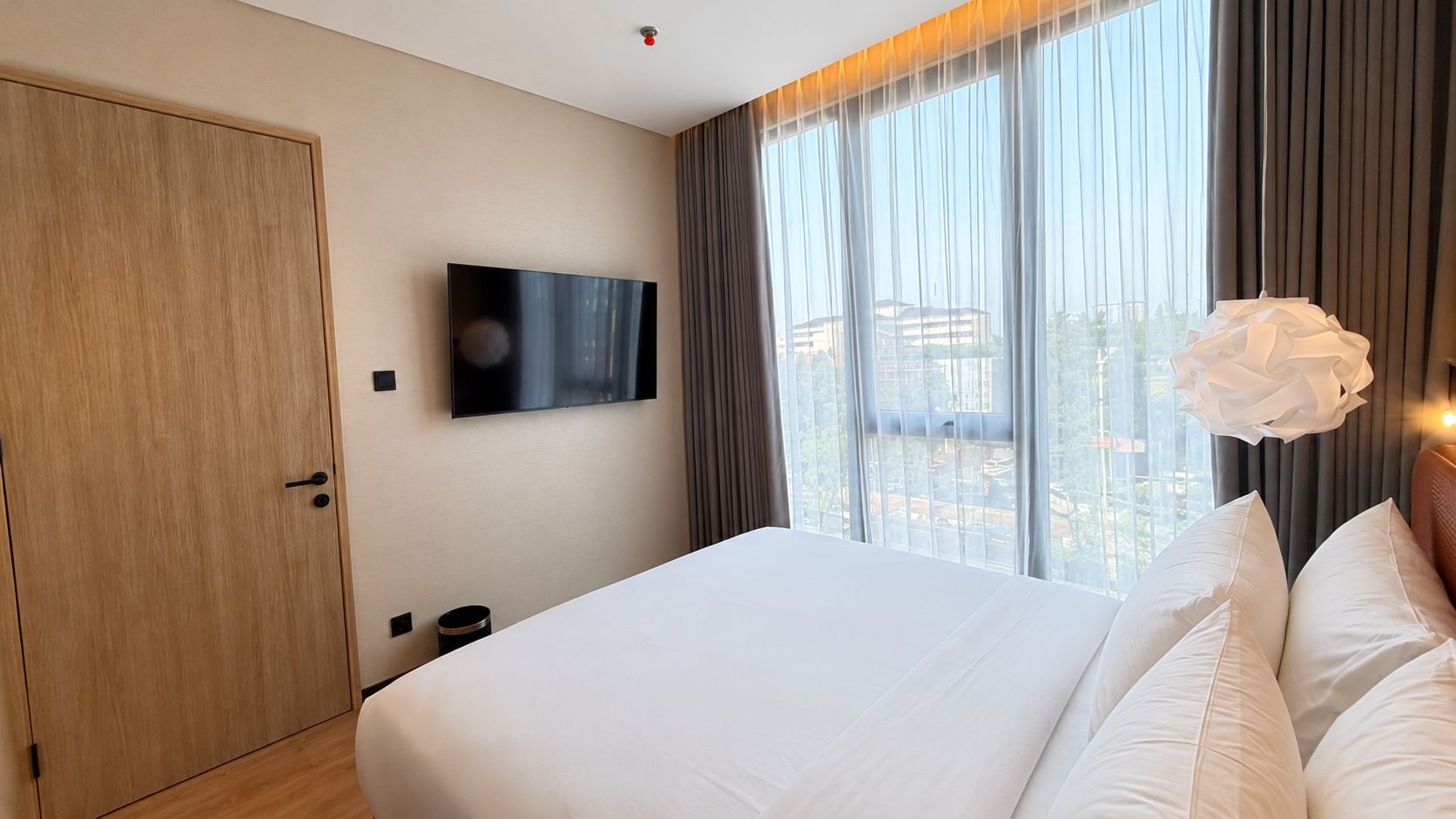 Quarto de hotel com uma cama grande, televisão de tela plana na parede e vista da cidade por grandes janelas.