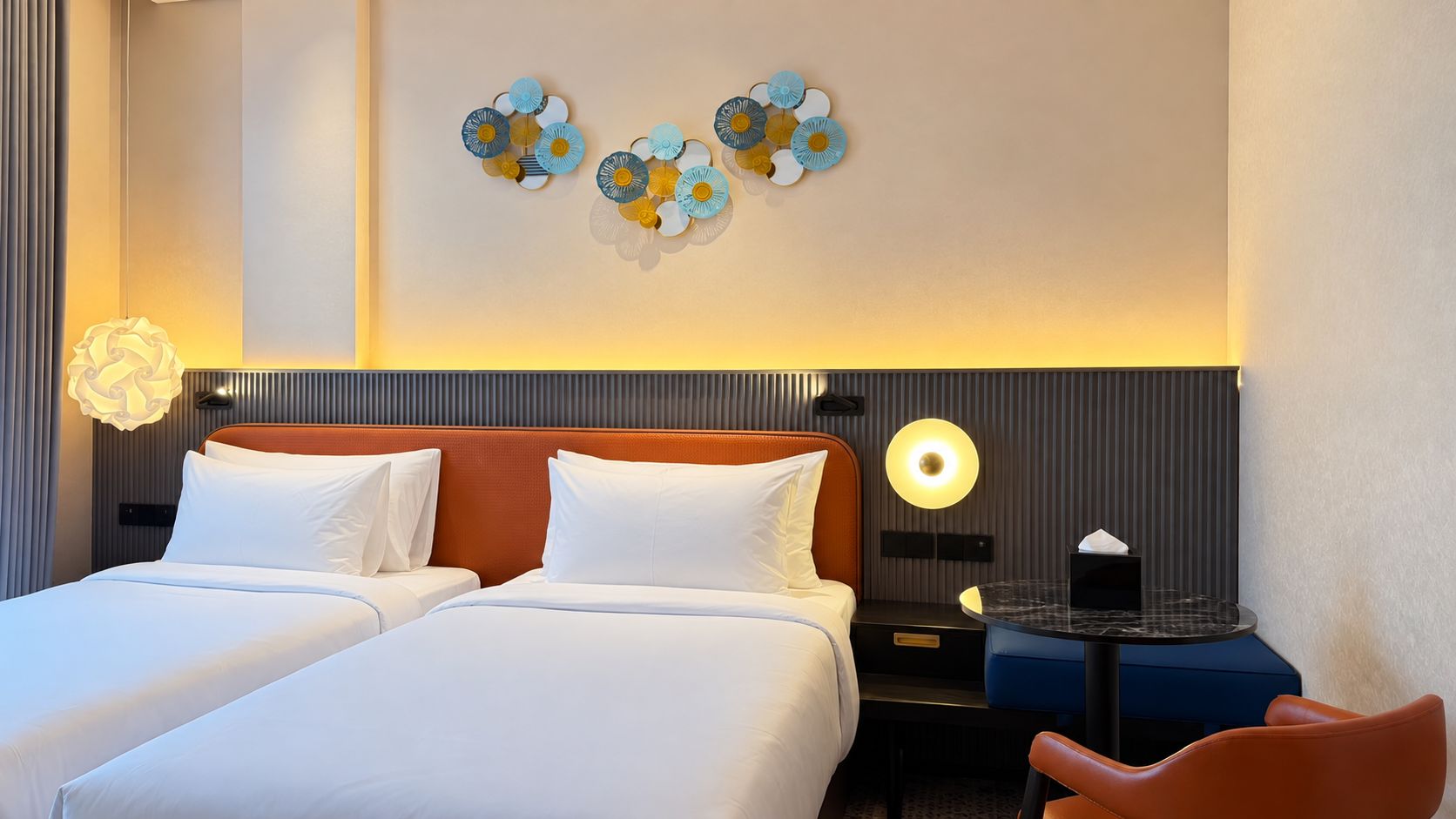 Una habitació d'hotel amb dos llits, una petita taula de nit, un escriptori amb una cadira i decoració mural.