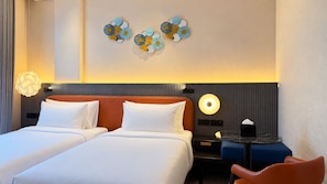 Habitación de hotel con dos camas, una mesita de noche, un escritorio con una silla y decoración en la pared.