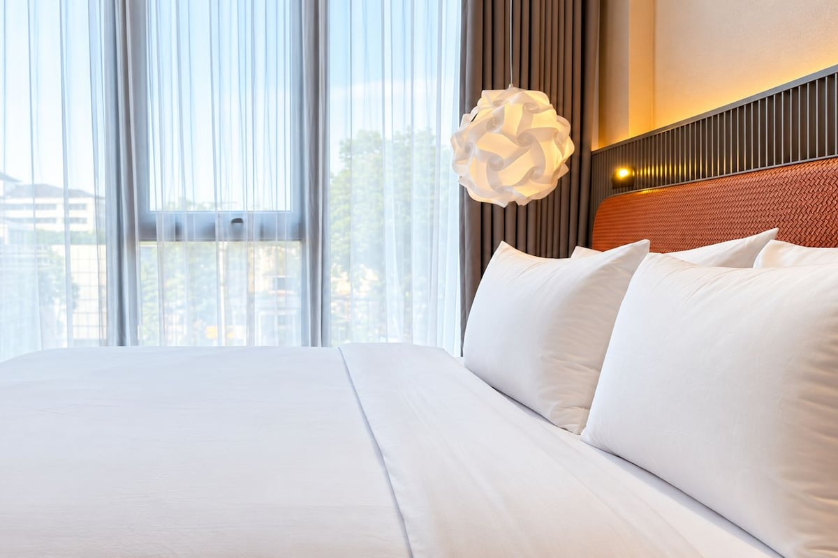 A hotel room with a large bed, a view of the city through the window, and a modern pendant light.