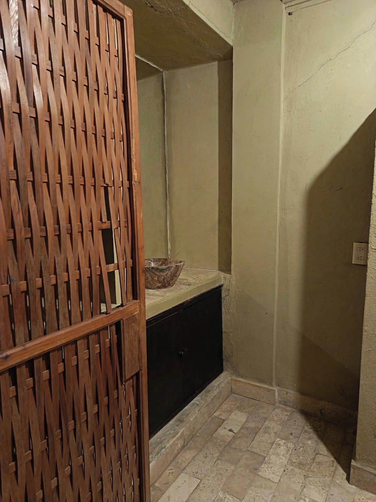 Een kamer met een houten scheiding, een stenen vloer en een kleine schaal op een aanrecht.