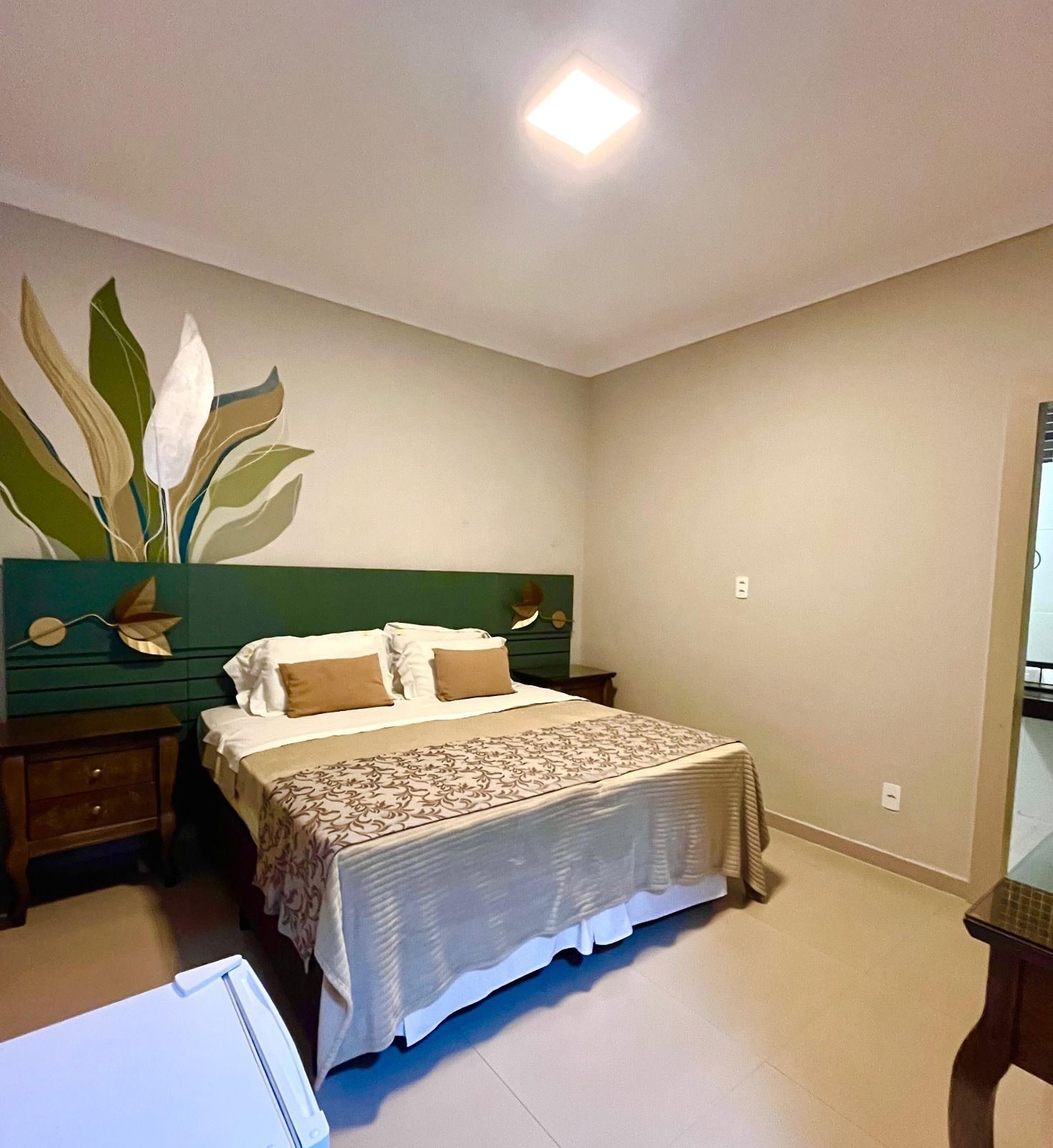 A bedroom with a bed, nightstands, a dresser, a mirror, and a wall with a leaf design.