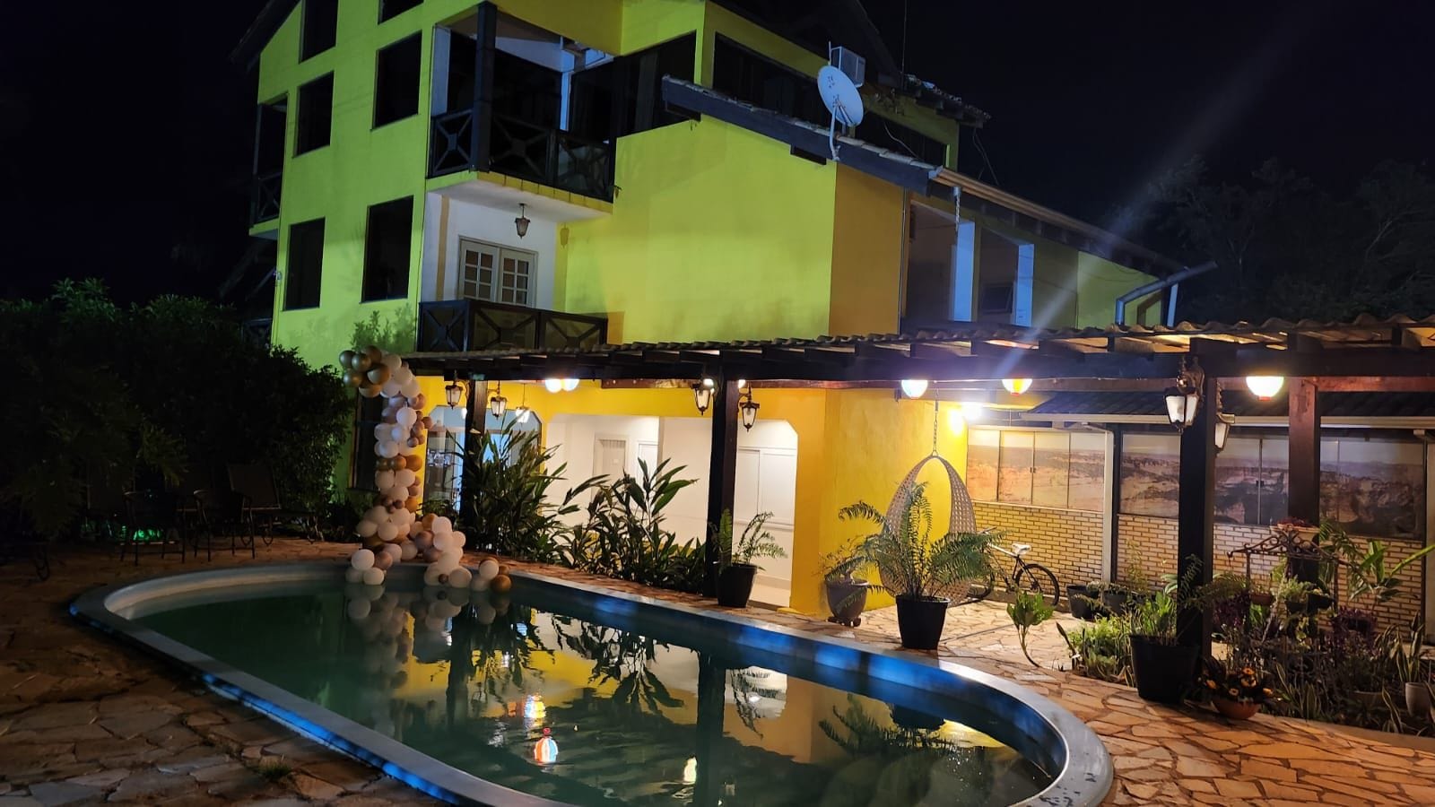 Un edificio de dos pisos con piscina, mobiliario exterior y plantas en macetas.