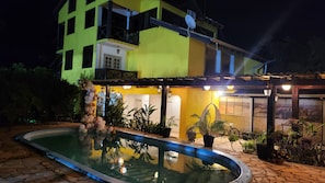 A two-story building with a swimming pool, outdoor seating, and potted plants. - Pousada Villa Guimarães  (CHAPADA DOS GUIMARÃES)