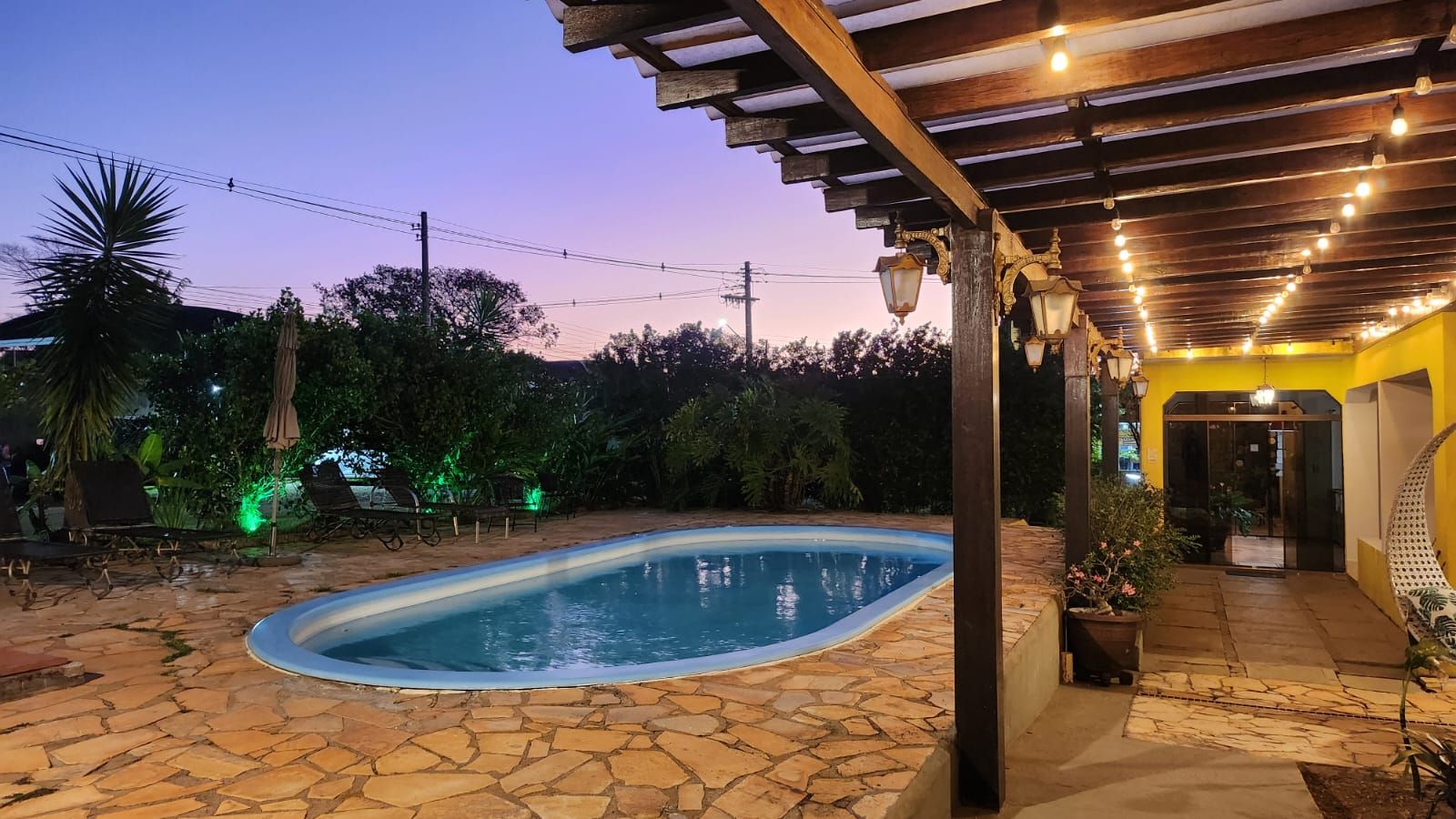 A swimming pool with stone flooring, surrounded by a covered patio area with hanging lights.