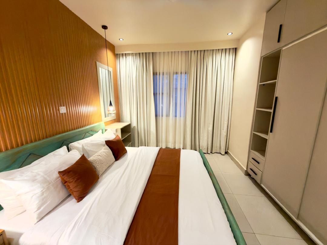A hotel room with a bed, a wardrobe, a window with curtains, and a headboard.