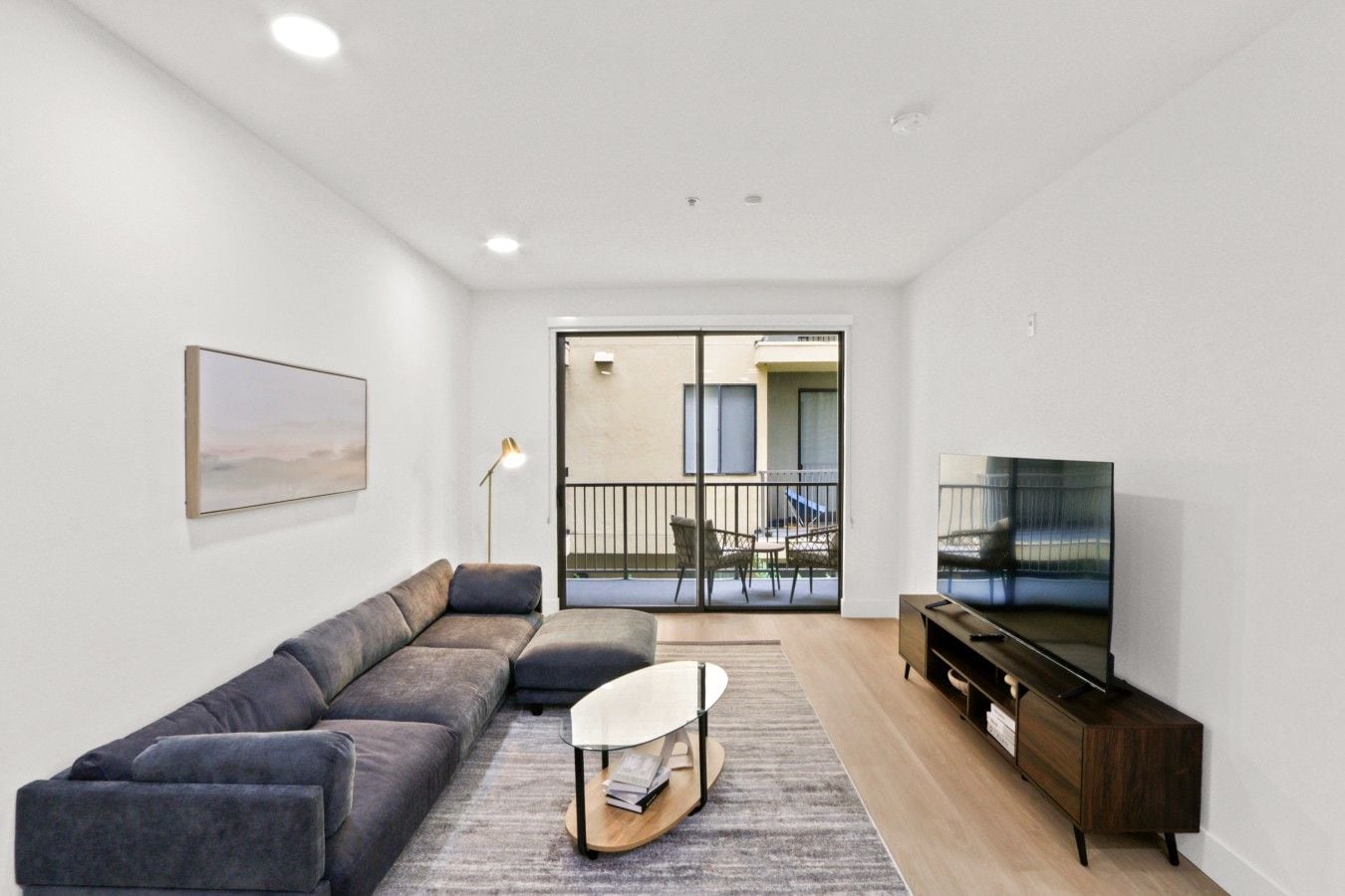 Una sala de estar moderna con un sofá, una mesa de centro, un televisor y un balcón con mobiliario exterior.