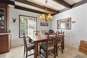 A dining area with a wooden table and chairs, a chandelier, and a window with blinds. - Boss's Cabin: Fireplace, Fire Pit & Deck, Sleeps 8 (Shaver Lake)