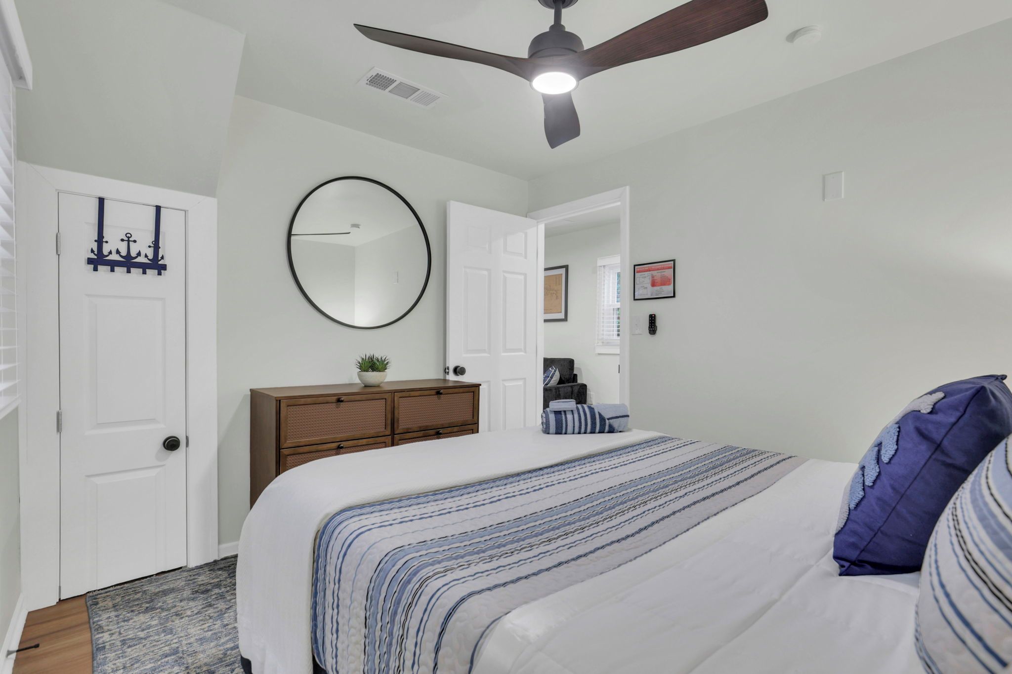 A bedroom with a bed, a dresser, a ceiling fan, and a round mirror.