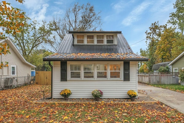 A small, single-story house with a gabled roof, a front porch, and a front yard with scattered leaves.