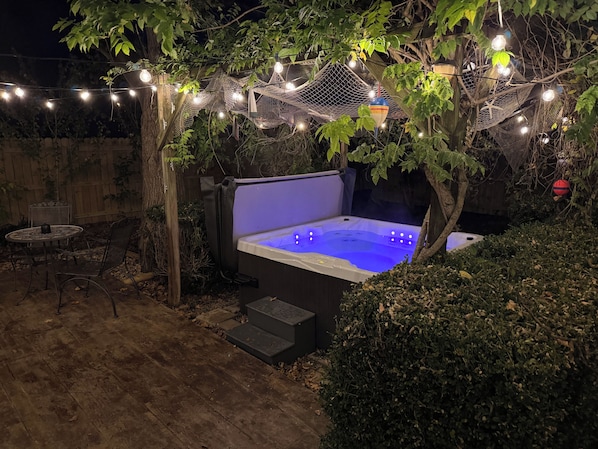 A hot tub under a netted canopy with string lights, surrounded by foliage and a wooden deck.