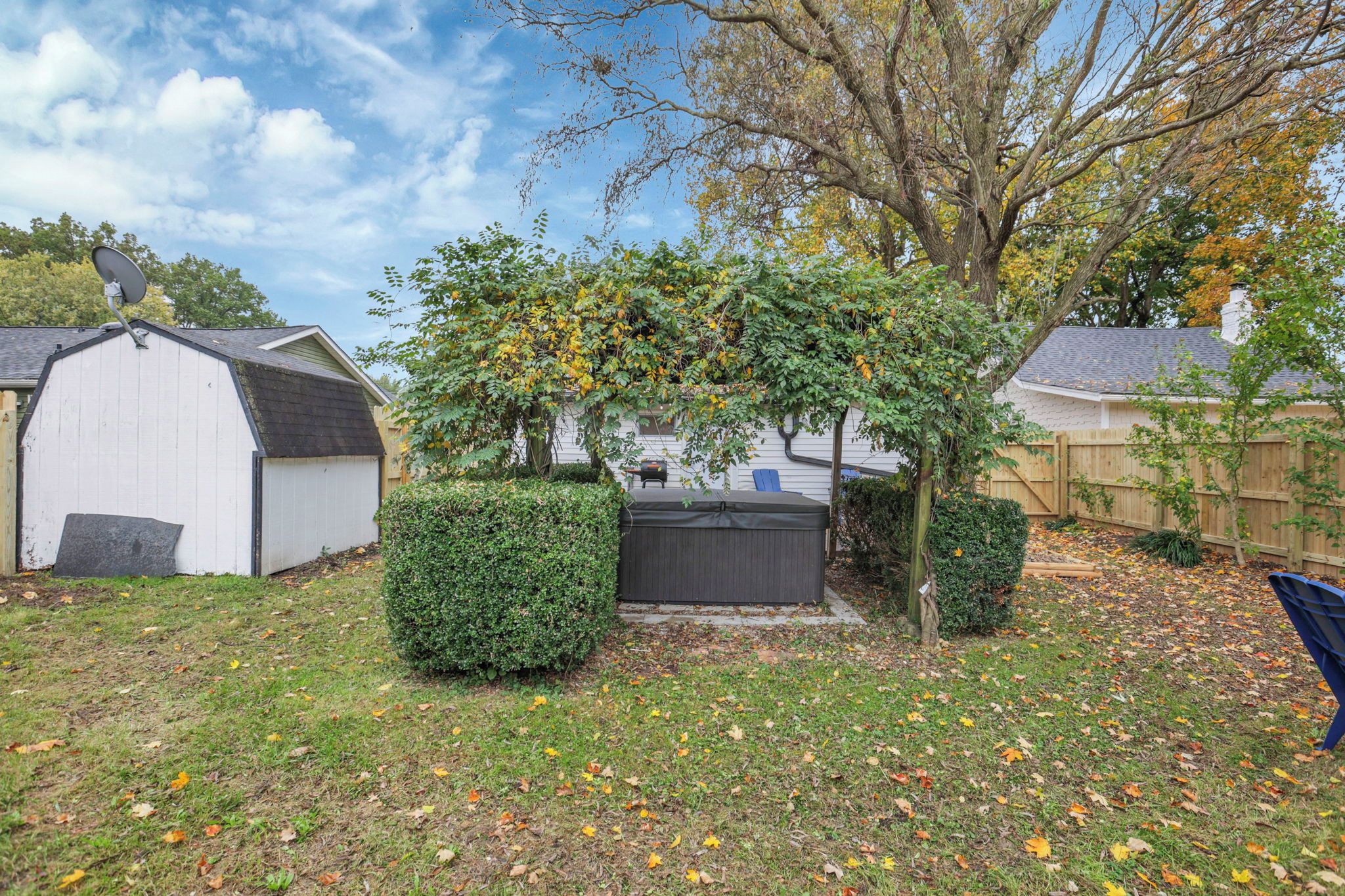 A backyard with a covered patio, a shed, and a tree with yellow leaves.