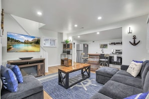 A modern living room with a wooden coffee table, grey sofas, and a large TV mounted on the wall.