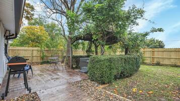 A backyard with a patio, a grill, and a wooden fence.