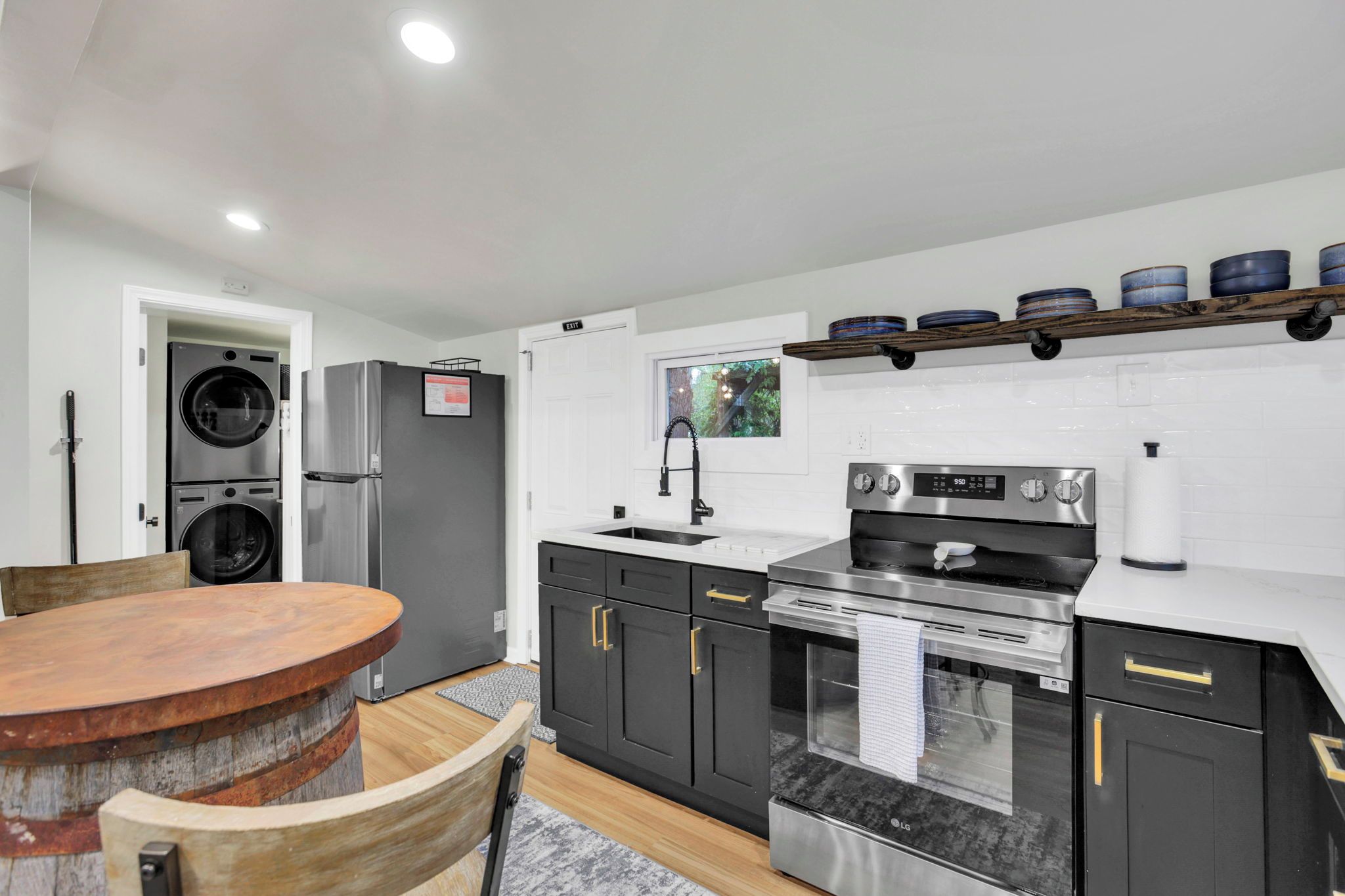 A modern kitchen with stainless steel appliances, a wooden dining table, and a window with a view of greenery.