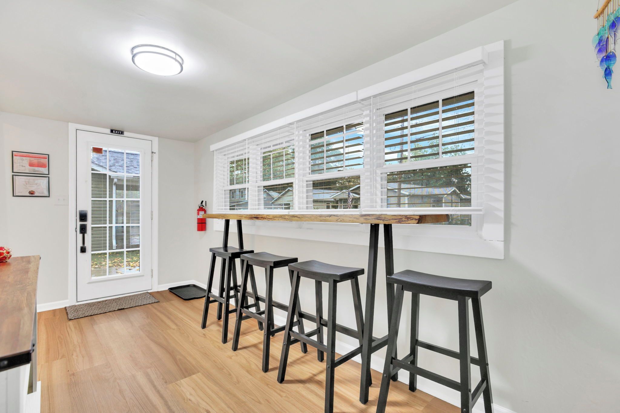 A kitchen with a wooden countertop, four black stools, a window with blinds, and a fire extinguisher on the wall.