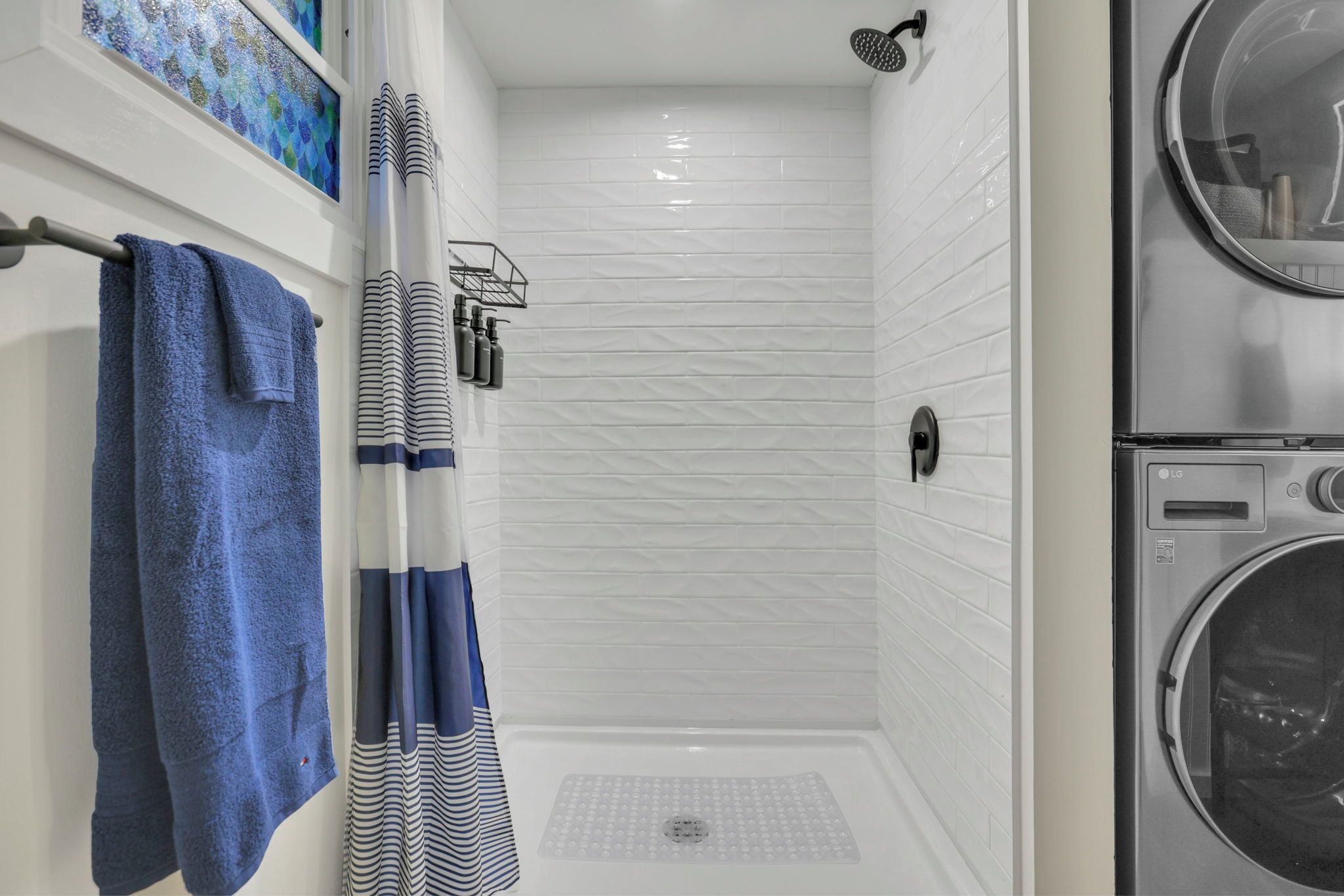 A bathroom with a shower, a towel rack with a blue towel, a striped shower curtain, and a washing machine.