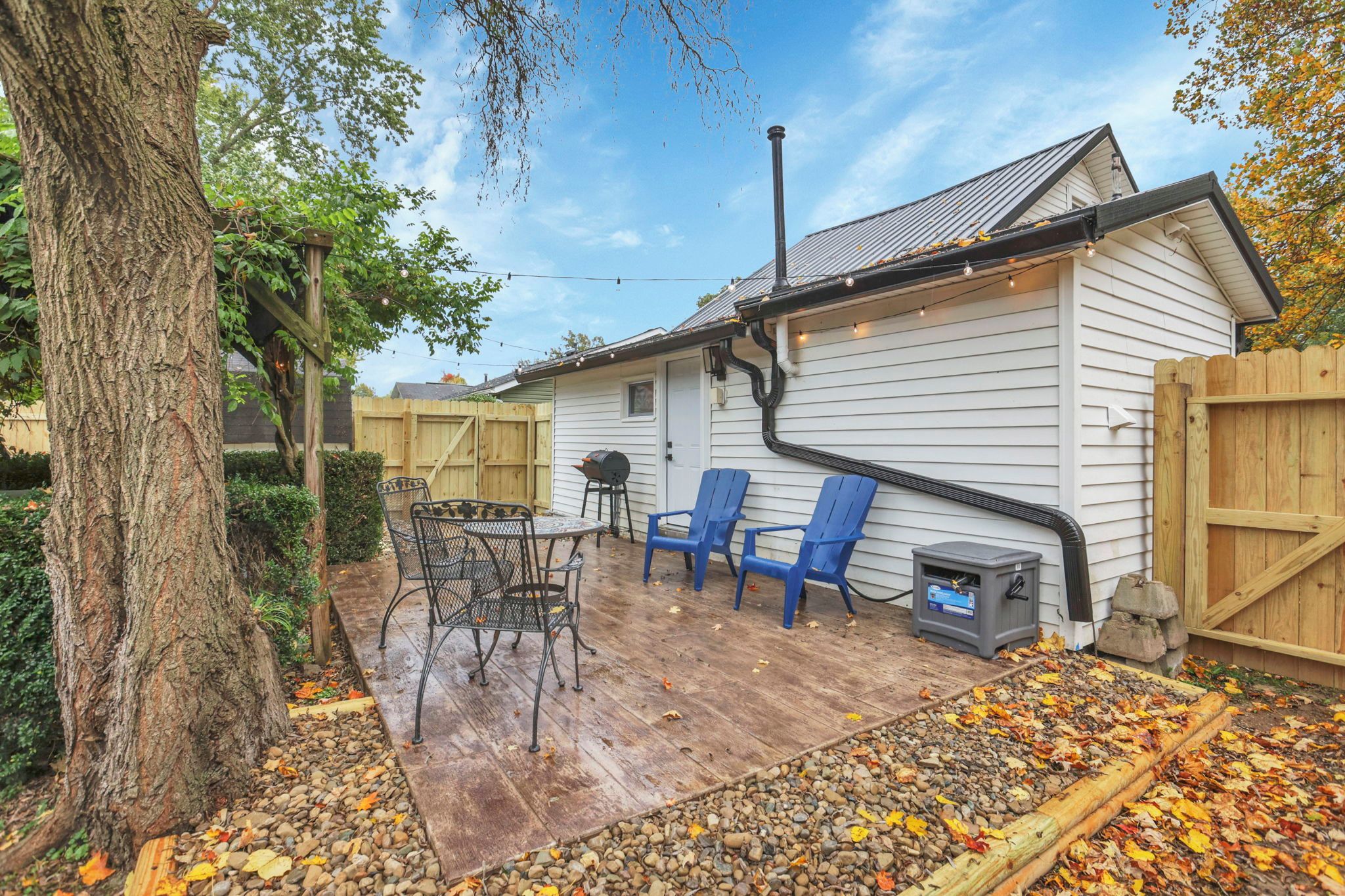 A wooden deck with a barbecue grill, outdoor seating, and a tree.