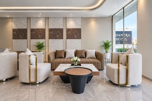 A modern hotel lobby with a sofa set, armchairs, a coffee table, and a decorative wall. - Hotel Vedantra (Bikaner)