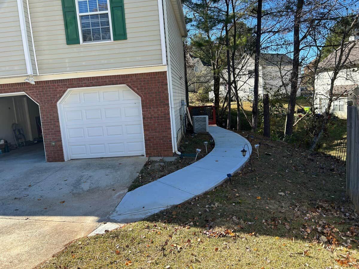 A residential property with a garage, a driveway, and a sidewalk leading to a house with a brick foundation.