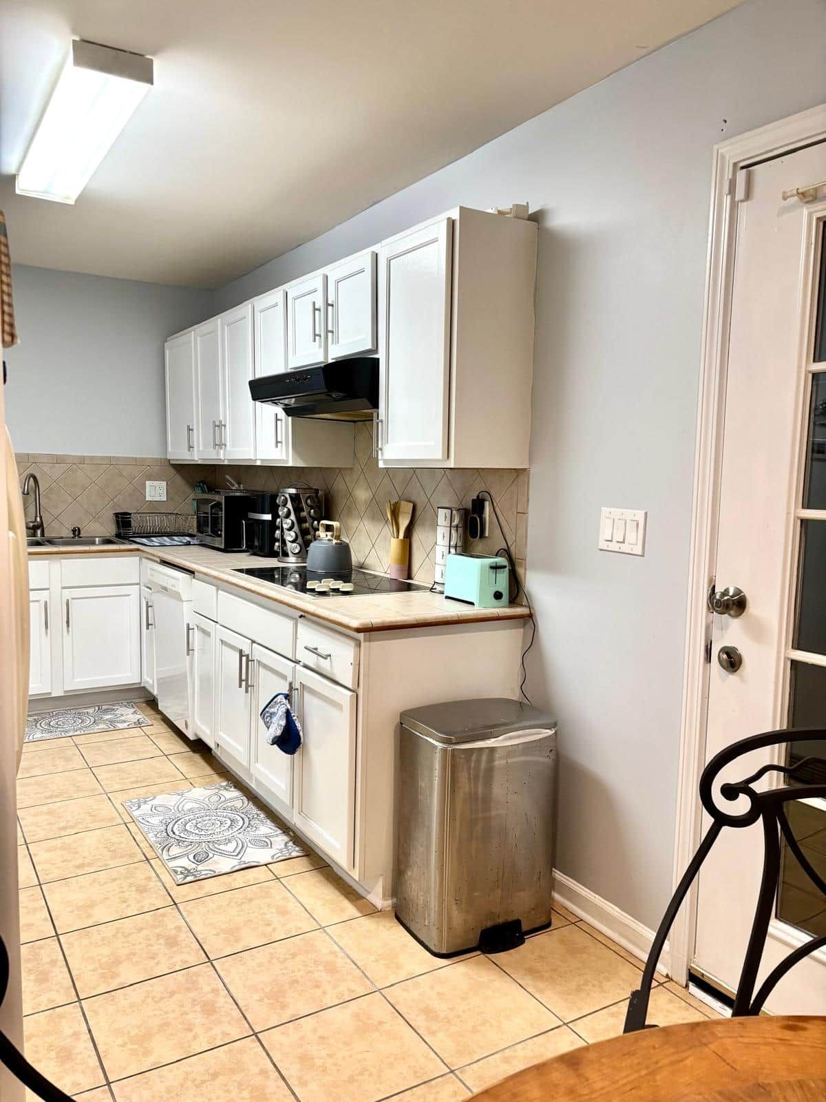A compact kitchen with white cabinets, a stainless steel toaster, and a tiled floor.