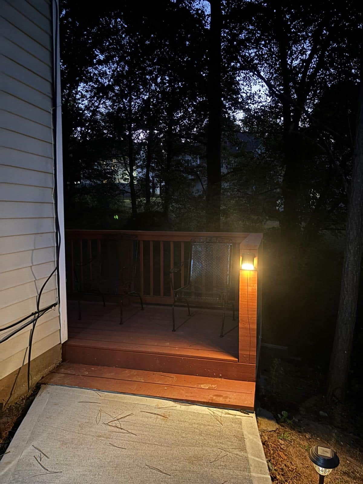 A wooden deck with metal chairs and a table, surrounded by trees.