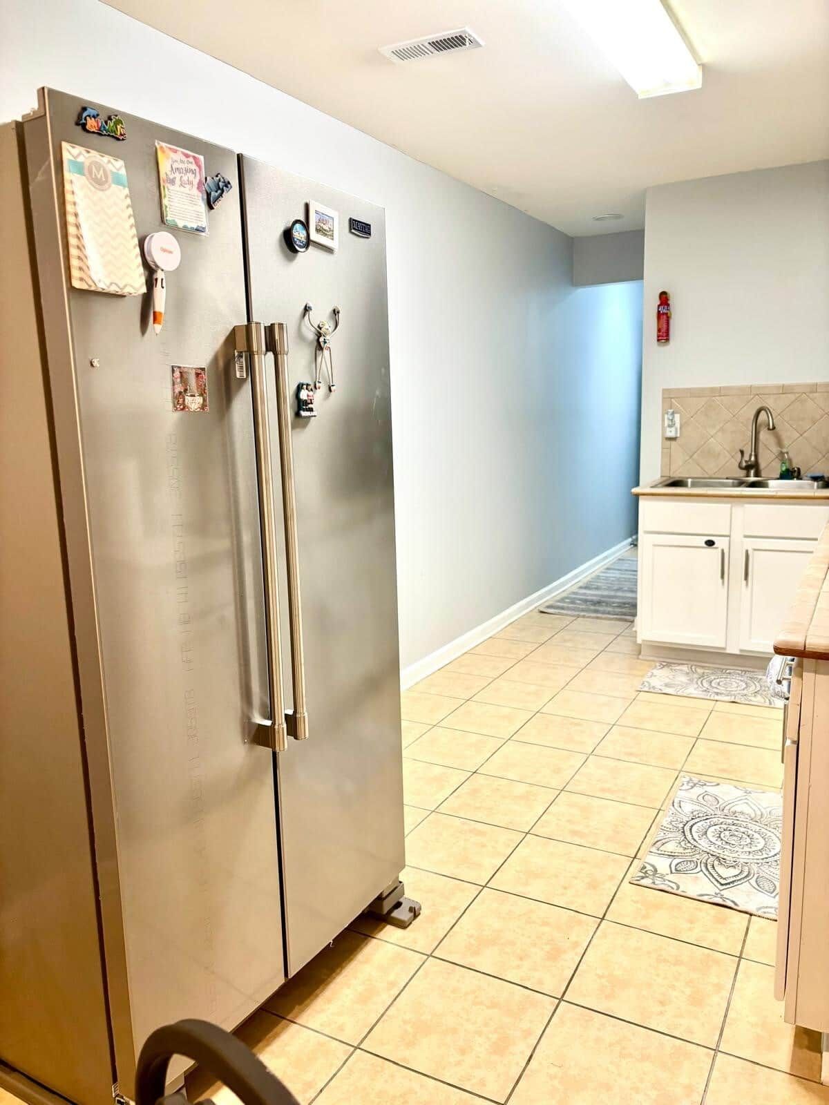 A kitchen with a stainless steel refrigerator, white cabinets, a sink, and a patterned rug.