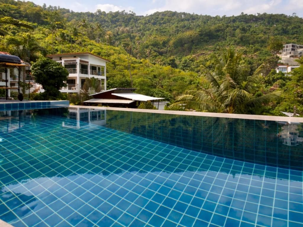 A swimming pool with a tiled edge, surrounded by lush greenery and hills in the background.