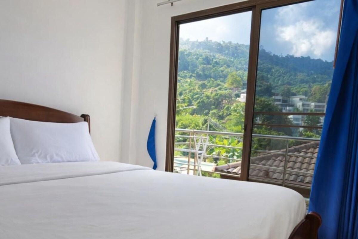 Een hotelkamer met een groot bed, uitzicht op een bergachtig landschap en een balkon met een hekwerk.