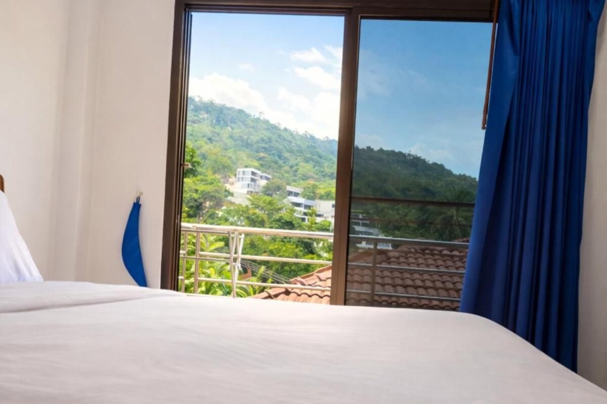 Een hotelkamer met een bed, uitzicht op een bergachtig landschap en een balkon met een leuning.