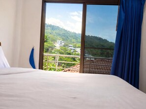 Een hotelkamer met een bed, uitzicht op een bergachtig landschap en een balkon met een leuning.