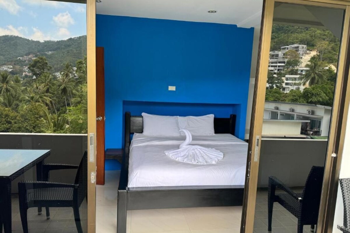 Een slaapkamer met een bed, een blauwe wand en uitzicht op een bergachtig gebied.