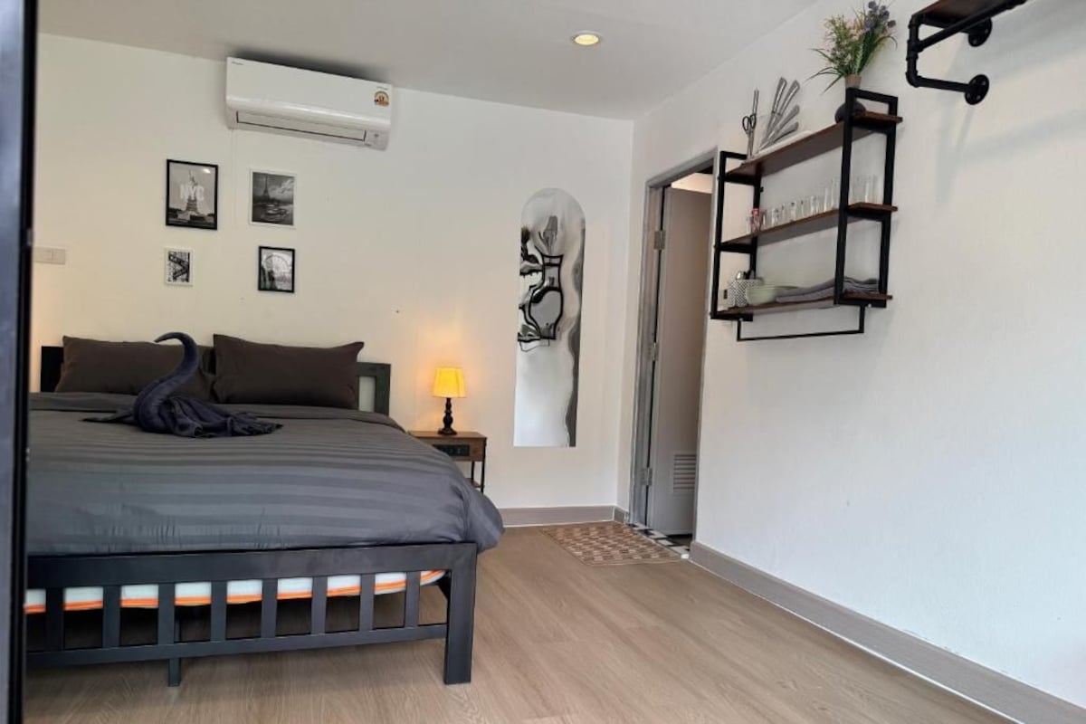 Een slaapkamer met een bed, bedlampje, wandplank en een deur naar een andere kamer.