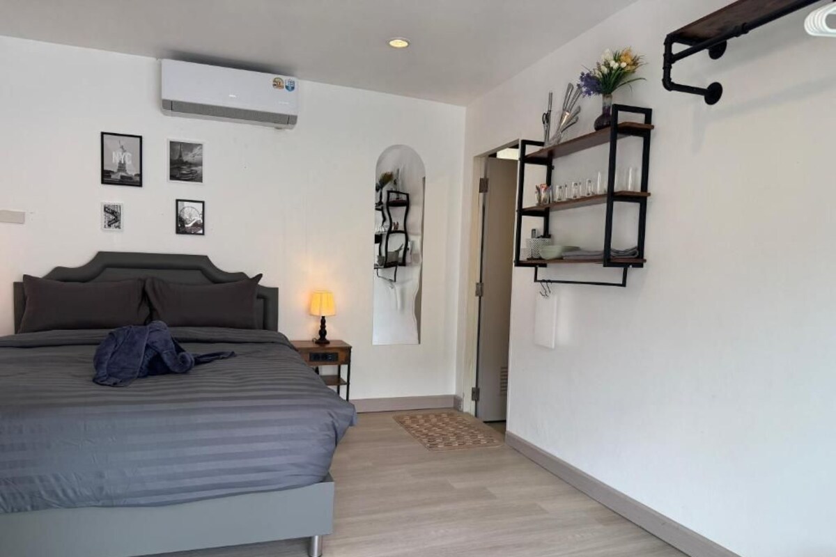 Een slaapkamer met een bed, nachtkastje, lamp, airconditioning en wandplanken.